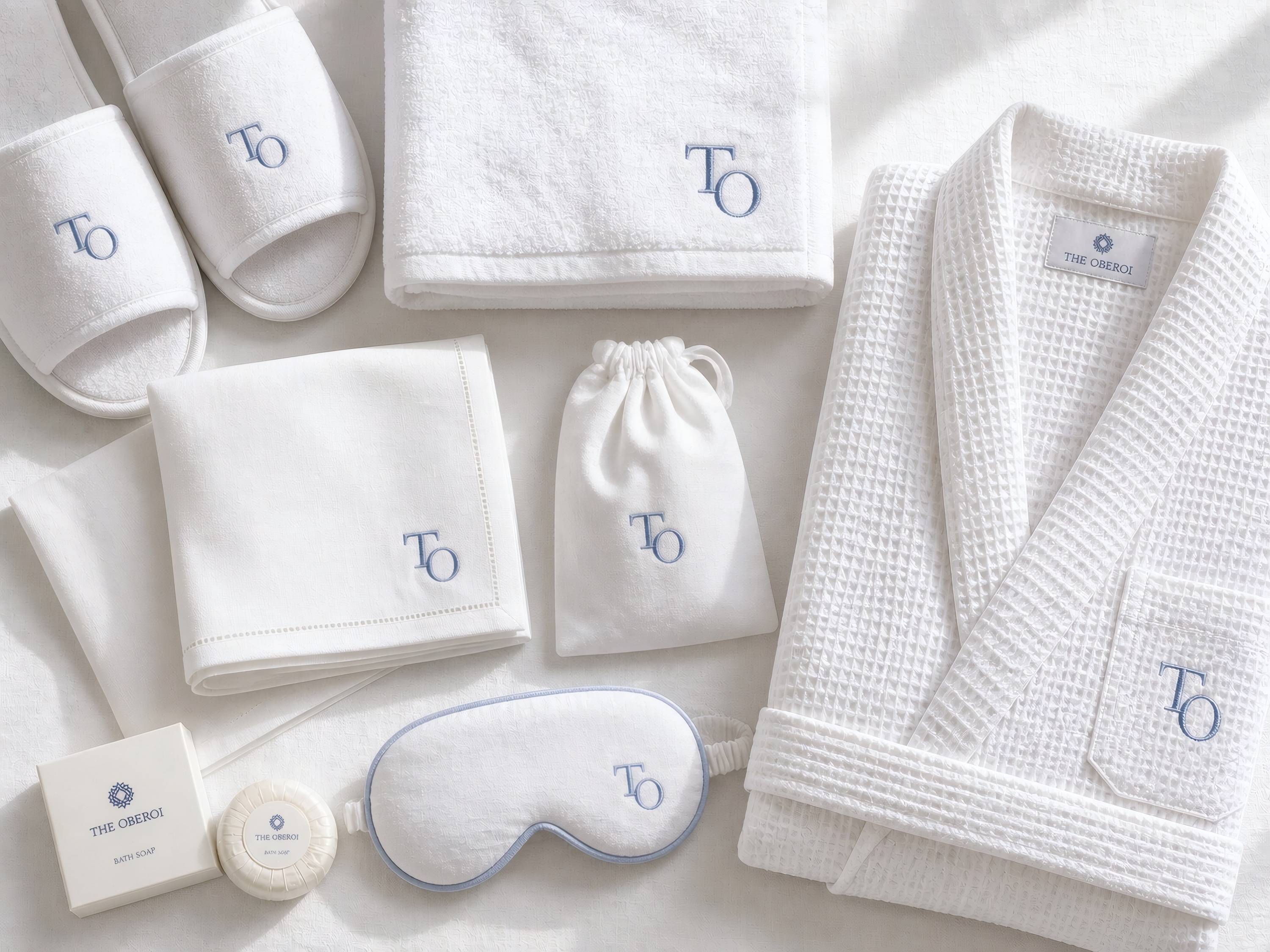 A flat-lay of white linen items embroidered with a hotel monogram in pale blue thread
